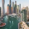 dubai Modern skyscrapers by a marina with boats and yachts in the water, seen from above with city buildings and waterfront paths.